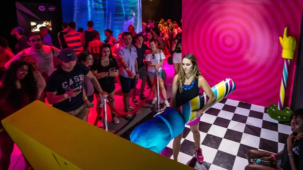 A woman holding a giant finger on a checkerboard floor.