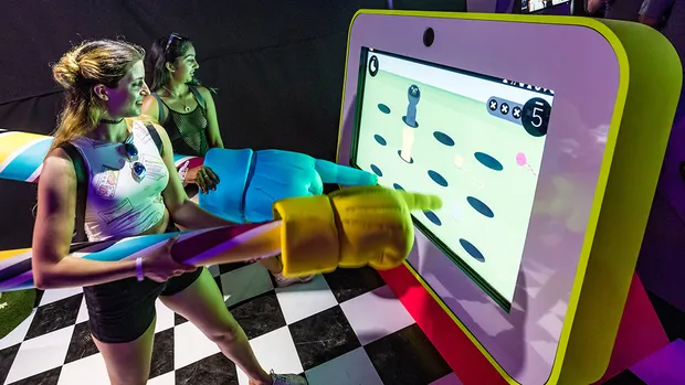 Two women holding giant fingers play a game on a tv.