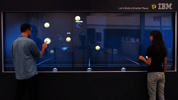 Two people playing with an interactive touch screen tennis application.