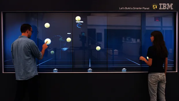 Two people playing with an interactive touch screen tennis application.